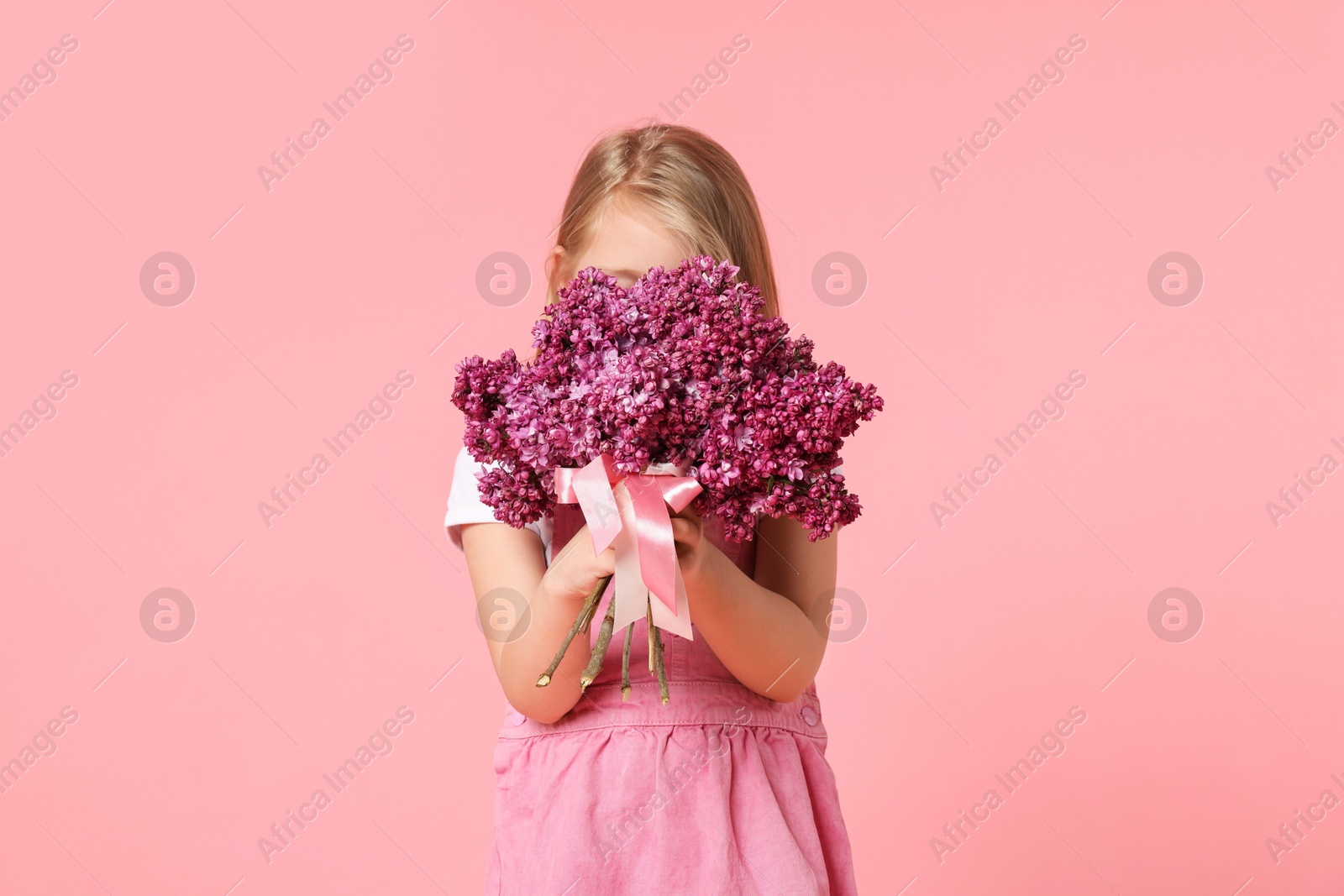 Little girl with bouquet of lilac flowers on pink background Photo of Little girl with bouquet of lilac flowers on pink background