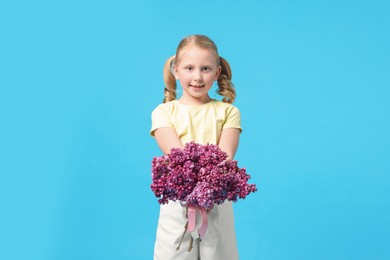 Photo of Little girl with bouquet of lilac flowers on light blue background