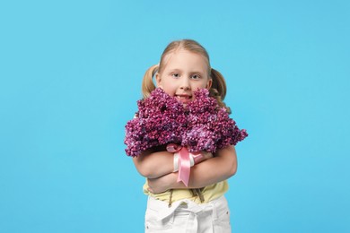 Photo of Little girl with bouquet of lilac flowers on light blue background