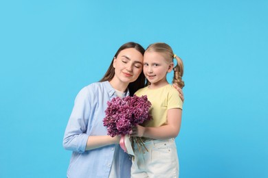 Photo of Mother and her daughter with bouquet of lilac flowers on light blue background