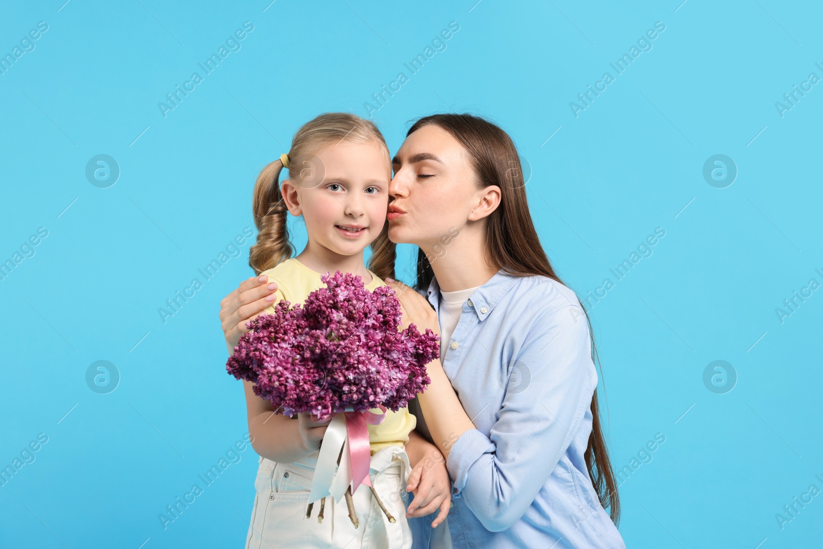 Mother and her daughter with bouquet of lilac flowers on light blue background Photo of Mother and her daughter with bouquet of lilac flowers on light blue background