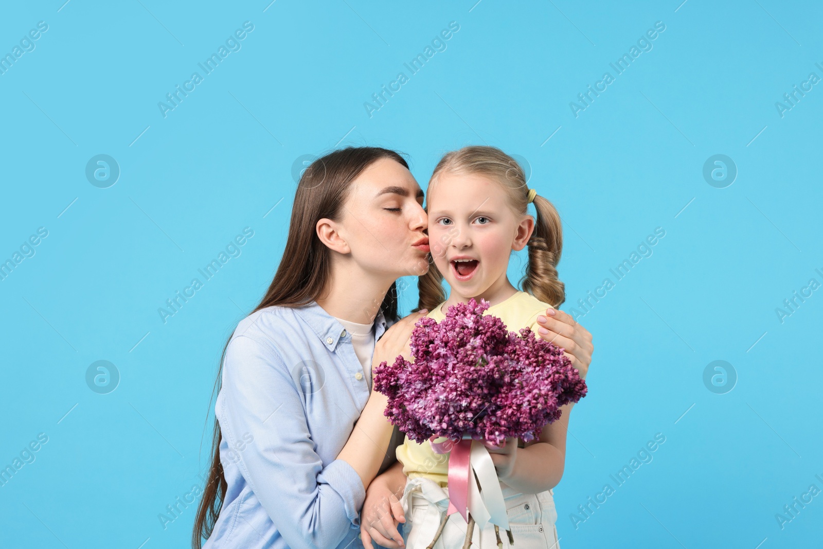 Mother and her daughter with bouquet of lilac flowers on light blue background Photo of Mother and her daughter with bouquet of lilac flowers on light blue background