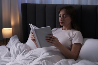 Photo of Beautiful woman reading book in bed at home