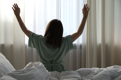 Photo of Woman stretching in bed at home, back view