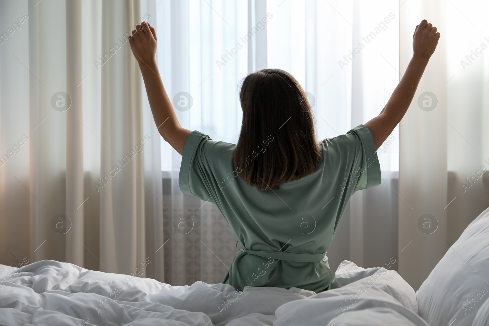 Woman stretching in bed at home, back view Photo of Woman stretching in bed at home, back view