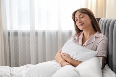Photo of Beautiful woman with pillow in bed at home, space for text