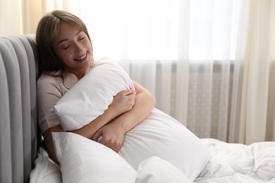 Photo of Beautiful woman with pillow in bed at home, space for text