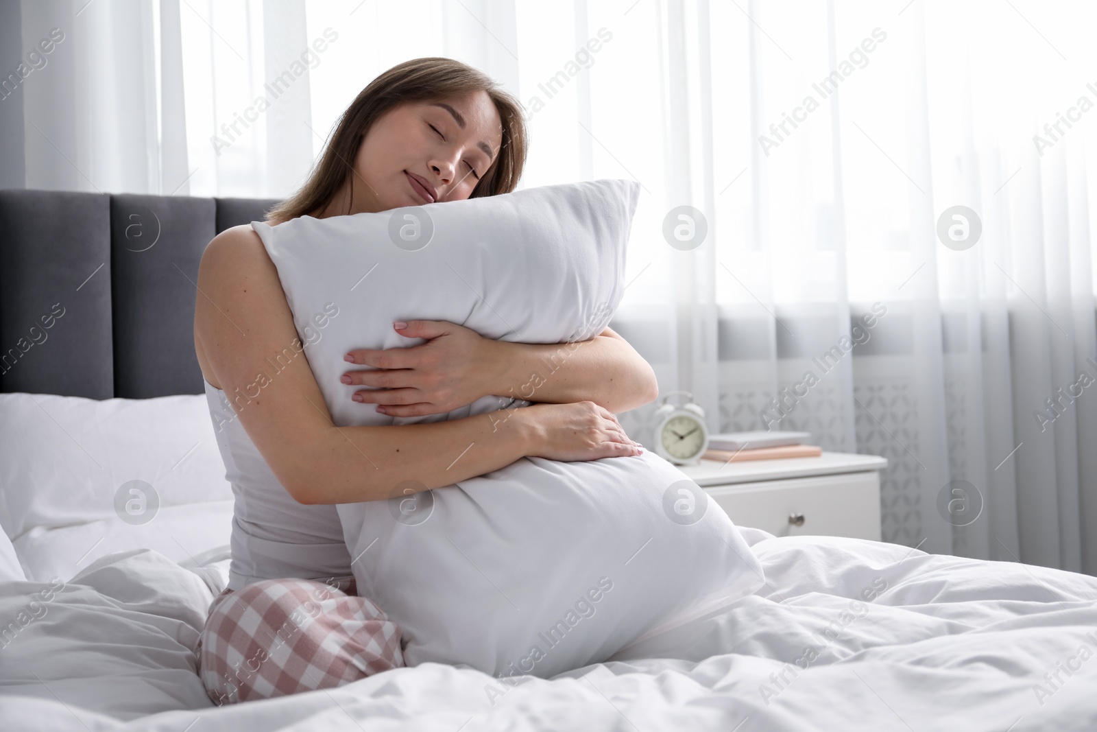 Beautiful woman with pillow on bed at home, space for text Photo of Beautiful woman with pillow on bed at home, space for text