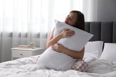 Photo of Beautiful woman with pillow on bed at home, space for text