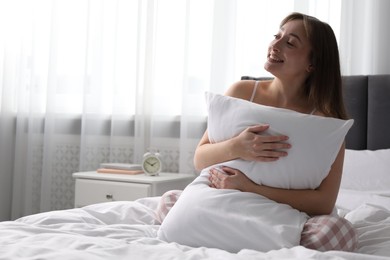 Photo of Beautiful woman with pillow on bed at home, space for text