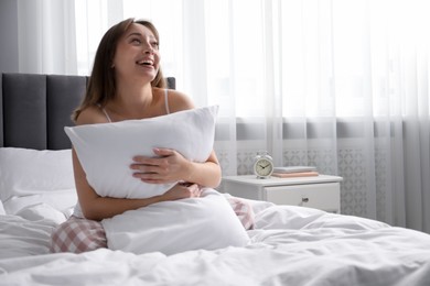 Photo of Beautiful woman with pillow on bed at home, space for text