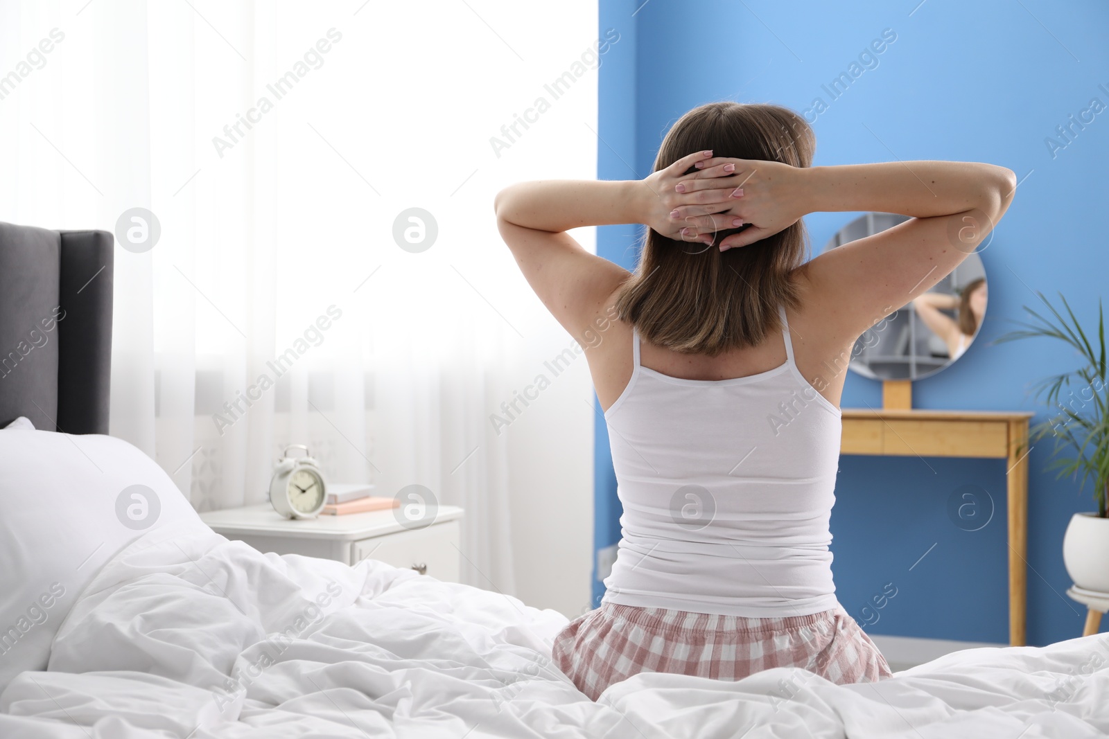 Woman stretching in bed at home, back view. Space for text Photo of Woman stretching in bed at home, back view. Space for text