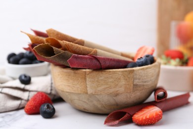 Photo of Tasty fruit leather rolls and berries on white table, closeup