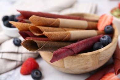 Photo of Tasty fruit leather rolls and berries on white table, closeup