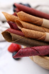 Photo of Tasty fruit leather rolls and berries on white table, closeup