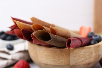 Photo of Tasty fruit leather rolls and berries on white table, closeup