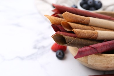 Photo of Tasty fruit leather rolls and berries on white marble table, closeup. Space for text
