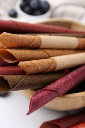 Photo of Tasty fruit leather rolls and berries on white table, closeup