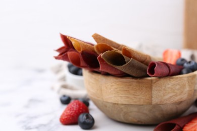 Photo of Tasty fruit leather rolls and berries on white marble table, closeup
