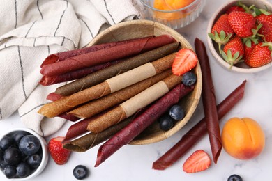 Photo of Tasty fruit leather rolls, apricots and berries on white marble table, flat lay