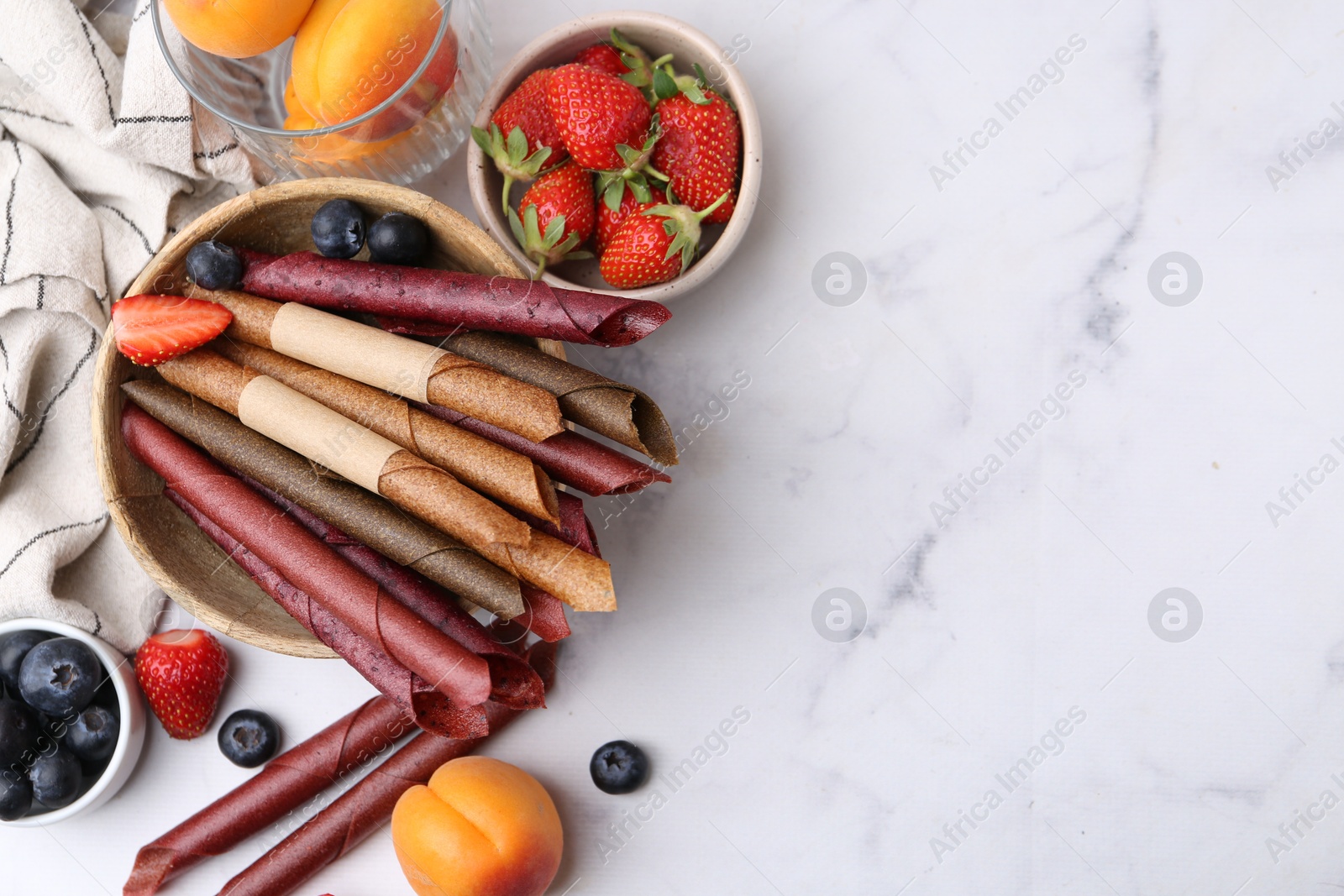 Tasty fruit leather rolls, apricots and berries on white marble table, flat lay. Space for text Photo of Tasty fruit leather rolls, apricots and berries on white marble table, flat lay. Space for text