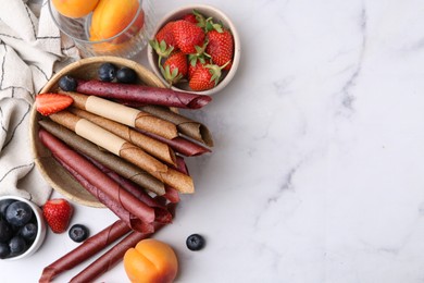 Photo of Tasty fruit leather rolls, apricots and berries on white marble table, flat lay. Space for text