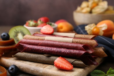 Photo of Tasty candied leather rolls, fruits and berries on wooden table, closeup