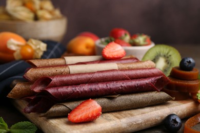 Photo of Tasty candied leather rolls, fruits and berries on wooden table, closeup