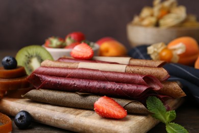 Photo of Tasty candied leather rolls, fruits and berries on wooden table, closeup