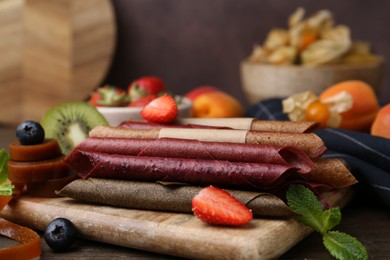 Photo of Tasty candied leather rolls, fruits and berries on wooden table, closeup