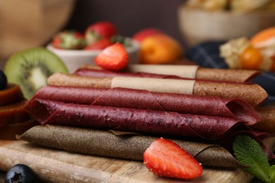 Photo of Tasty candied leather rolls, fruits and berries on wooden table, closeup