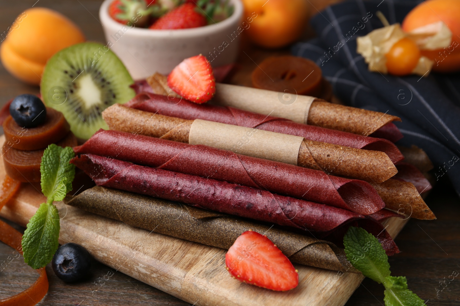 Tasty candied leather rolls, fruits and berries on wooden table, closeup Photo of Tasty candied leather rolls, fruits and berries on wooden table, closeup