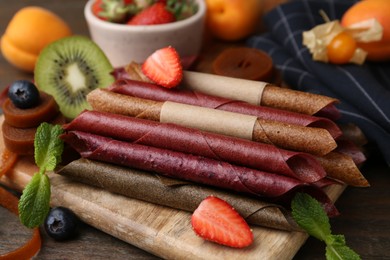 Photo of Tasty candied leather rolls, fruits and berries on wooden table, closeup