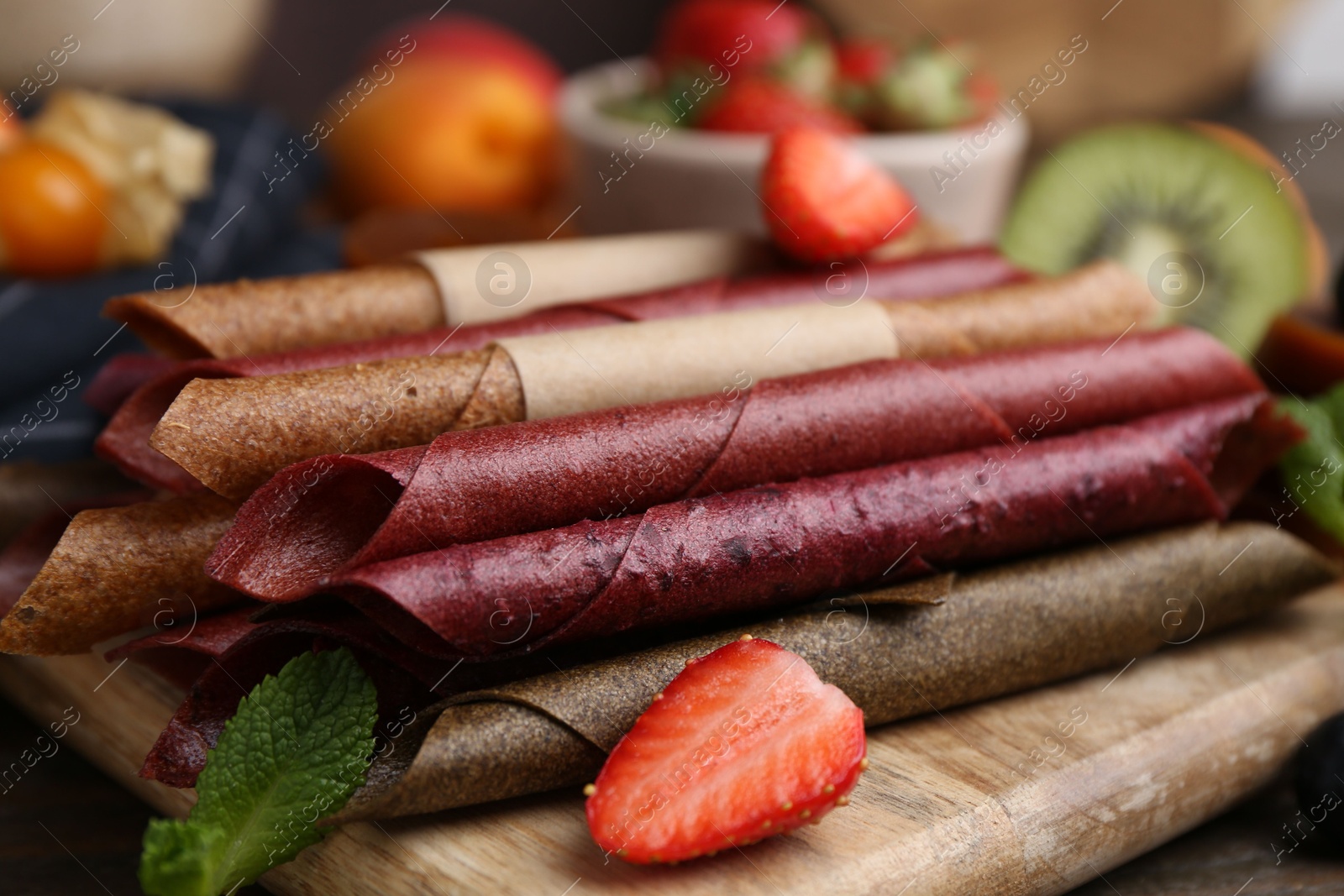 Tasty candied leather rolls, fruits and berries on wooden table, closeup Photo of Tasty candied leather rolls, fruits and berries on wooden table, closeup