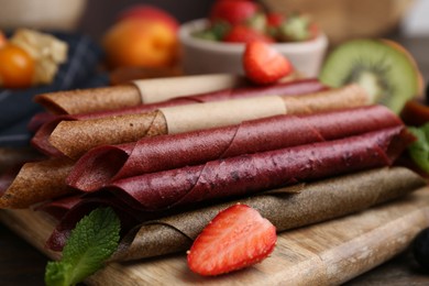 Photo of Tasty candied leather rolls, fruits and berries on wooden table, closeup