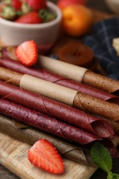 Photo of Tasty candied leather rolls, fruits and berries on wooden table, closeup