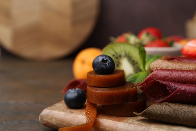 Photo of Tasty candied leather rolls, fruits and berries on wooden table, closeup. Space for text