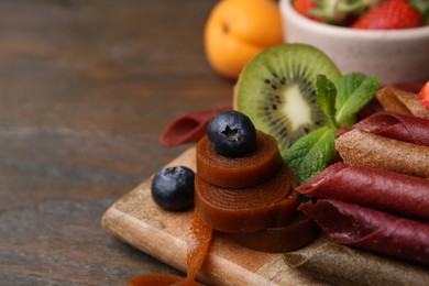 Photo of Tasty candied leather rolls, fruits and berries on wooden table, closeup. Space for text