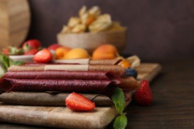 Photo of Tasty candied leather rolls, fruits and berries on wooden table, closeup