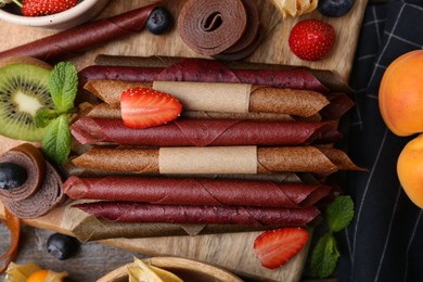 Photo of Tasty candied leather rolls, fruits and berries on wooden table, flat lay
