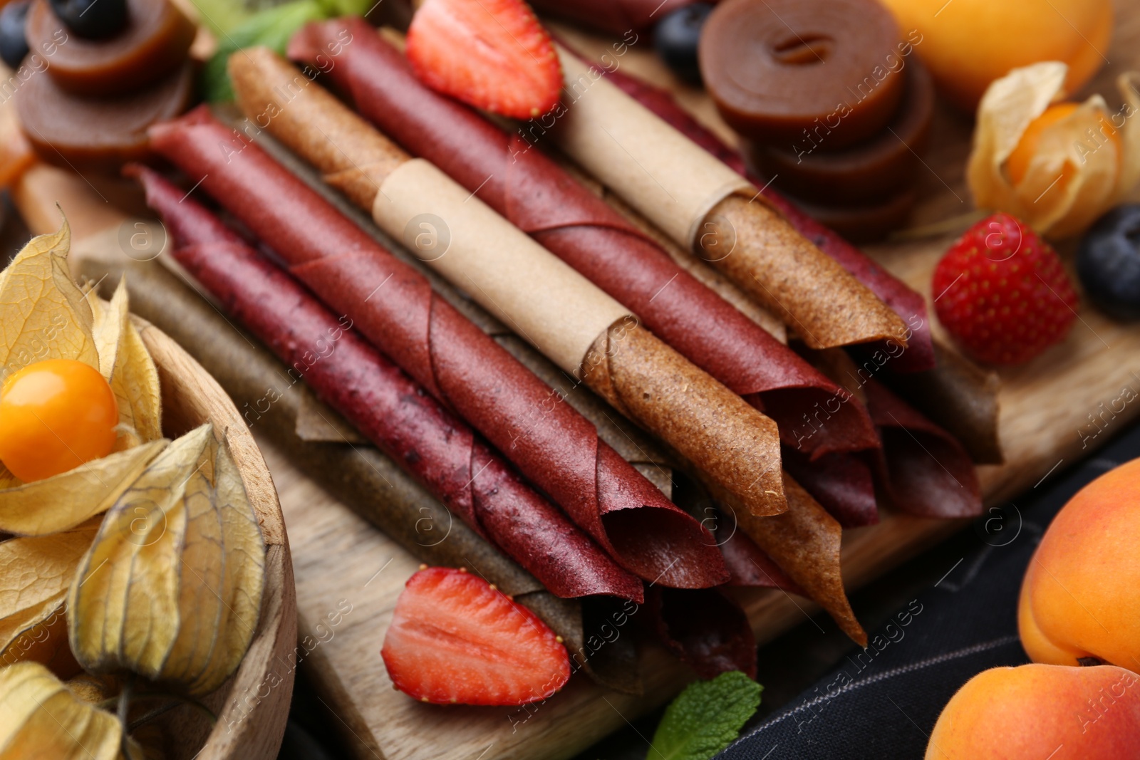 Tasty candied leather rolls, fruits and berries on wooden table, closeup Photo of Tasty candied leather rolls, fruits and berries on wooden table, closeup