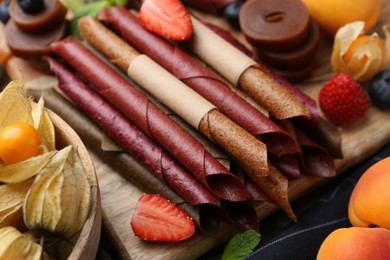 Photo of Tasty candied leather rolls, fruits and berries on wooden table, closeup