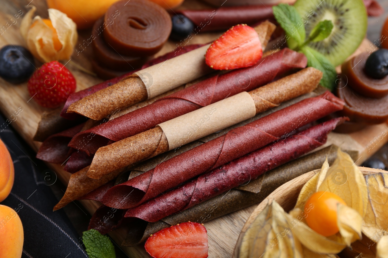 Tasty candied leather rolls, fruits and berries on wooden table, closeup Photo of Tasty candied leather rolls, fruits and berries on wooden table, closeup