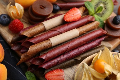 Photo of Tasty candied leather rolls, fruits and berries on wooden table, closeup
