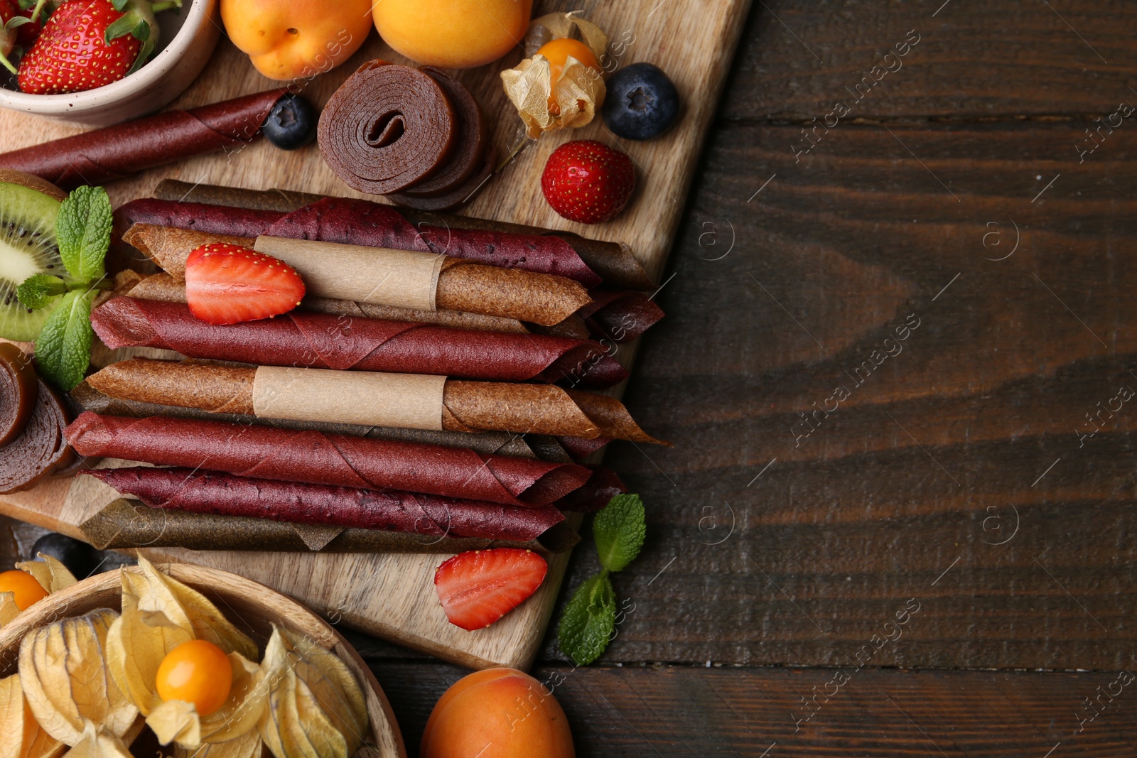 Tasty candied leather rolls, fruits and berries on wooden table, flat lay. Space for text Photo of Tasty candied leather rolls, fruits and berries on wooden table, flat lay. Space for text