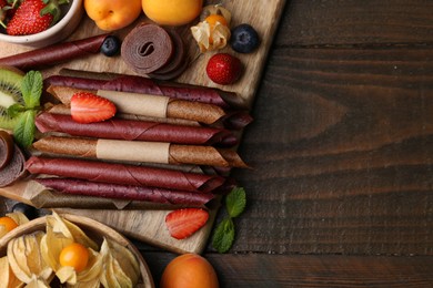 Photo of Tasty candied leather rolls, fruits and berries on wooden table, flat lay. Space for text
