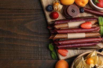 Photo of Tasty candied leather rolls, fruits and berries on wooden table, flat lay. Space for text