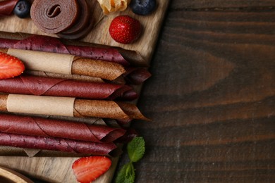 Photo of Tasty candied leather rolls, fruits and berries on wooden table, flat lay. Space for text