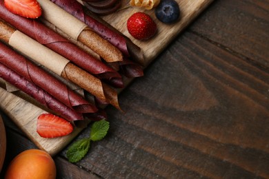Photo of Tasty candied leather rolls, fruits and berries on wooden table, flat lay. Space for text
