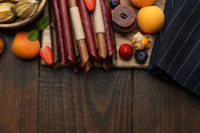 Photo of Tasty candied leather rolls, fruits and berries on wooden table, flat lay. Space for text